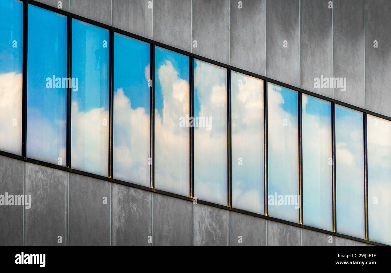 Reflet du ciel bleu et des nuages blancs dans les fenêtres d'un bâtiment en béton gris Banque D'Images