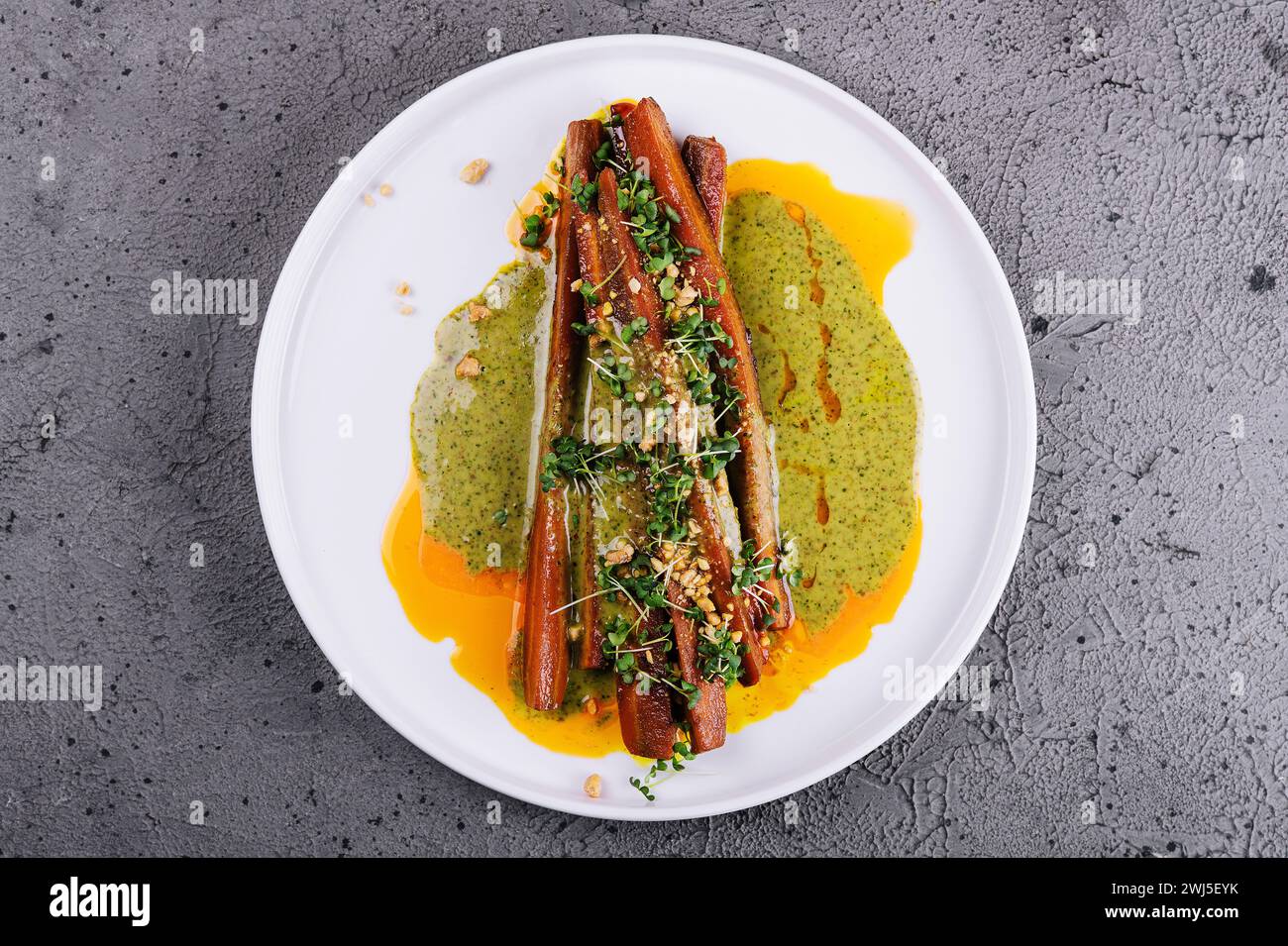 Les carottes rôties sont servies sur une assiette en grès blanc accompagnée d’un pesto Banque D'Images