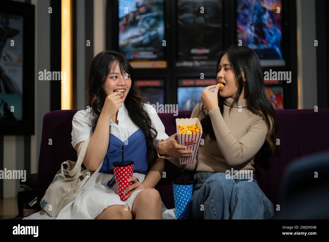 Deux jeunes femmes asiatiques mangeant du pop-corn et attendant de regarder un film devant le cinéma Banque D'Images