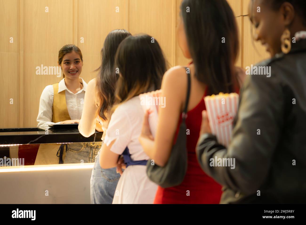 Jeune femme asiatique debout dans la file pour acheter des billets de cinéma et dans la main pop-corn et boire, souriant vendeur de billets servant. Banque D'Images