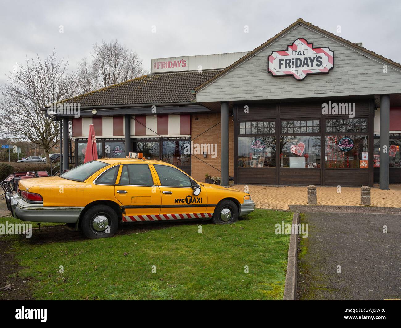 Façade de TGI Fridays, un restaurant à thème américain, Sixfields, Northampton, Royaume-Uni ; avec un taxi américain jaune à l'extérieur Banque D'Images