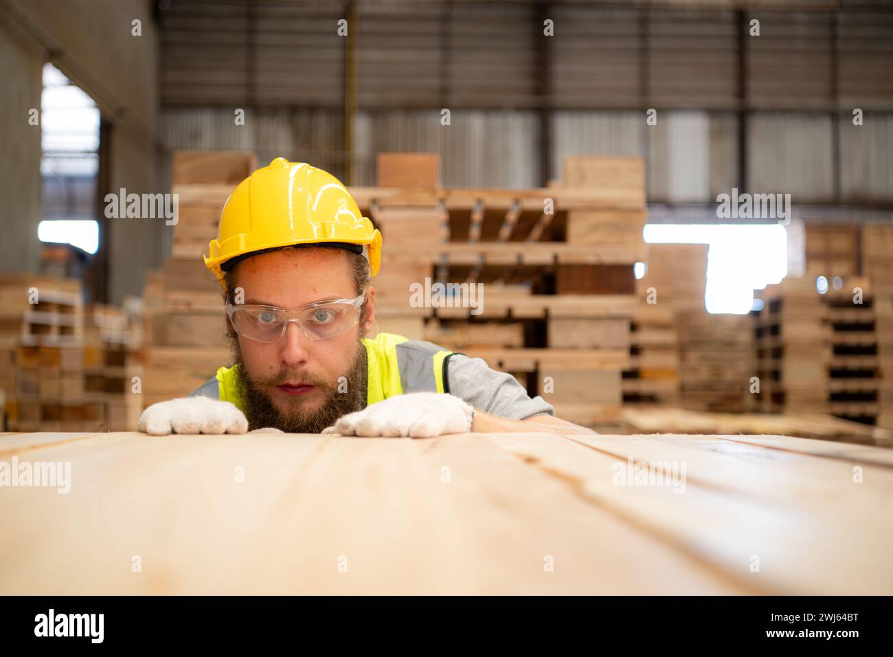 Un mec menuisier portant un casque et des lunettes inspecte un élément de travail terminé dans une industrie du bois. Banque D'Images