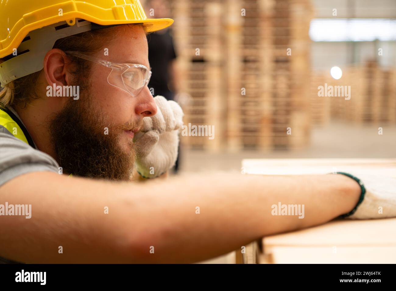 Un mec menuisier portant un casque et des lunettes inspecte un élément de travail terminé dans une industrie du bois. Banque D'Images