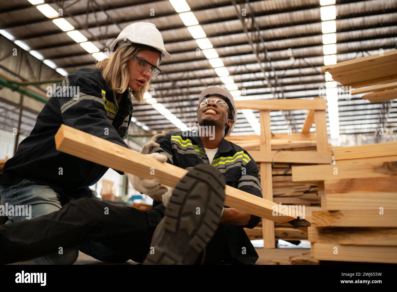 Travailleur d'entrepôt de bois blessé à la jambe, les collègues aident et soutiennent pour aller à la salle de premiers soins pour le traitement. Banque D'Images