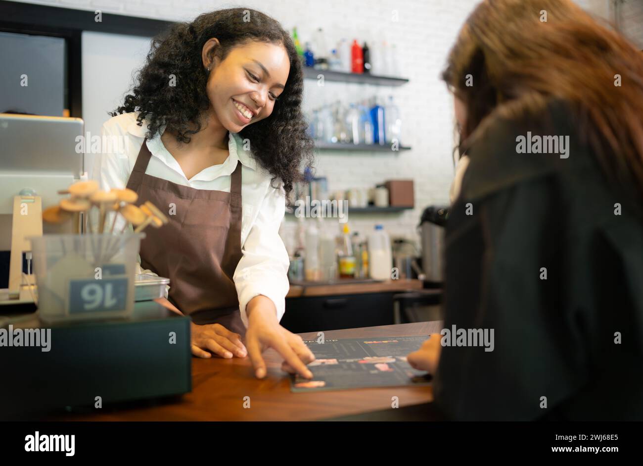 Les clients sélectionnent des articles de café. avec une jeune femme barista travaillant au comptoir du café Banque D'Images