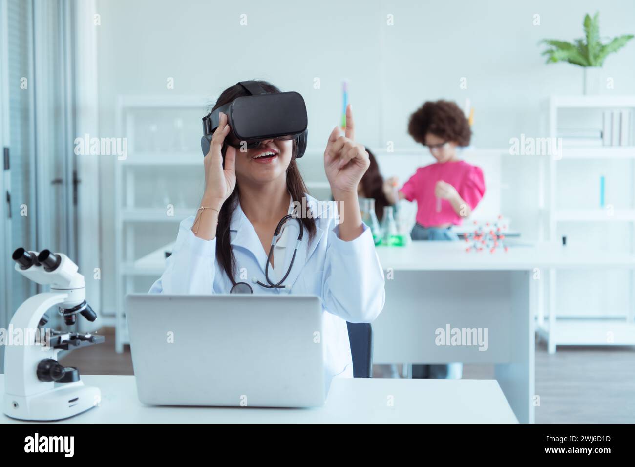 Jeune scientifique utilisant un casque de réalité virtuelle pendant que des collègues travaillent en arrière-plan au laboratoire Banque D'Images