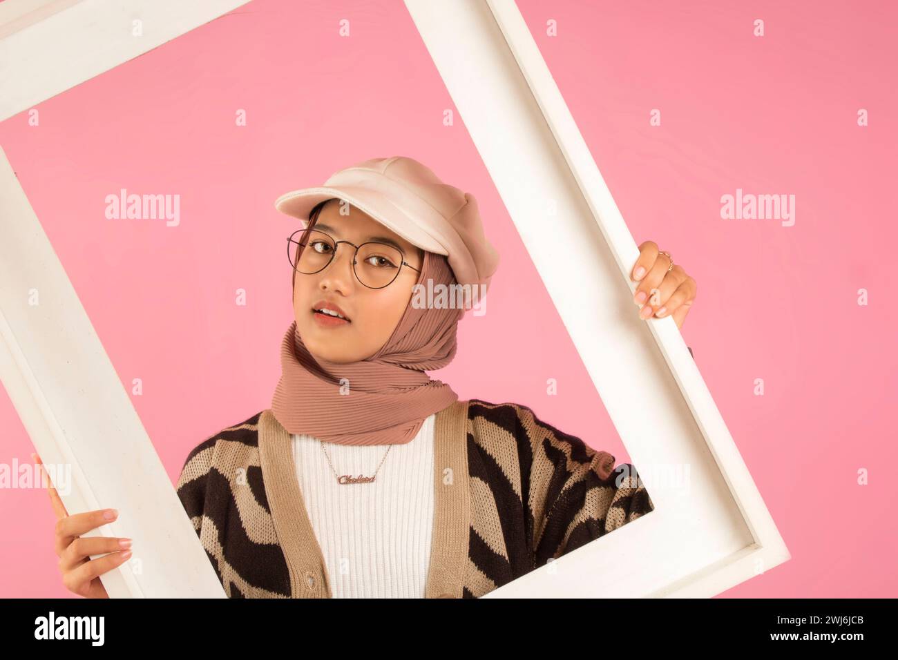 gros plan d'une adolescente asiatique posant avec un cadre blanc et portant le hijab, le chapeau blanc et les lunettes. fond blanc Banque D'Images