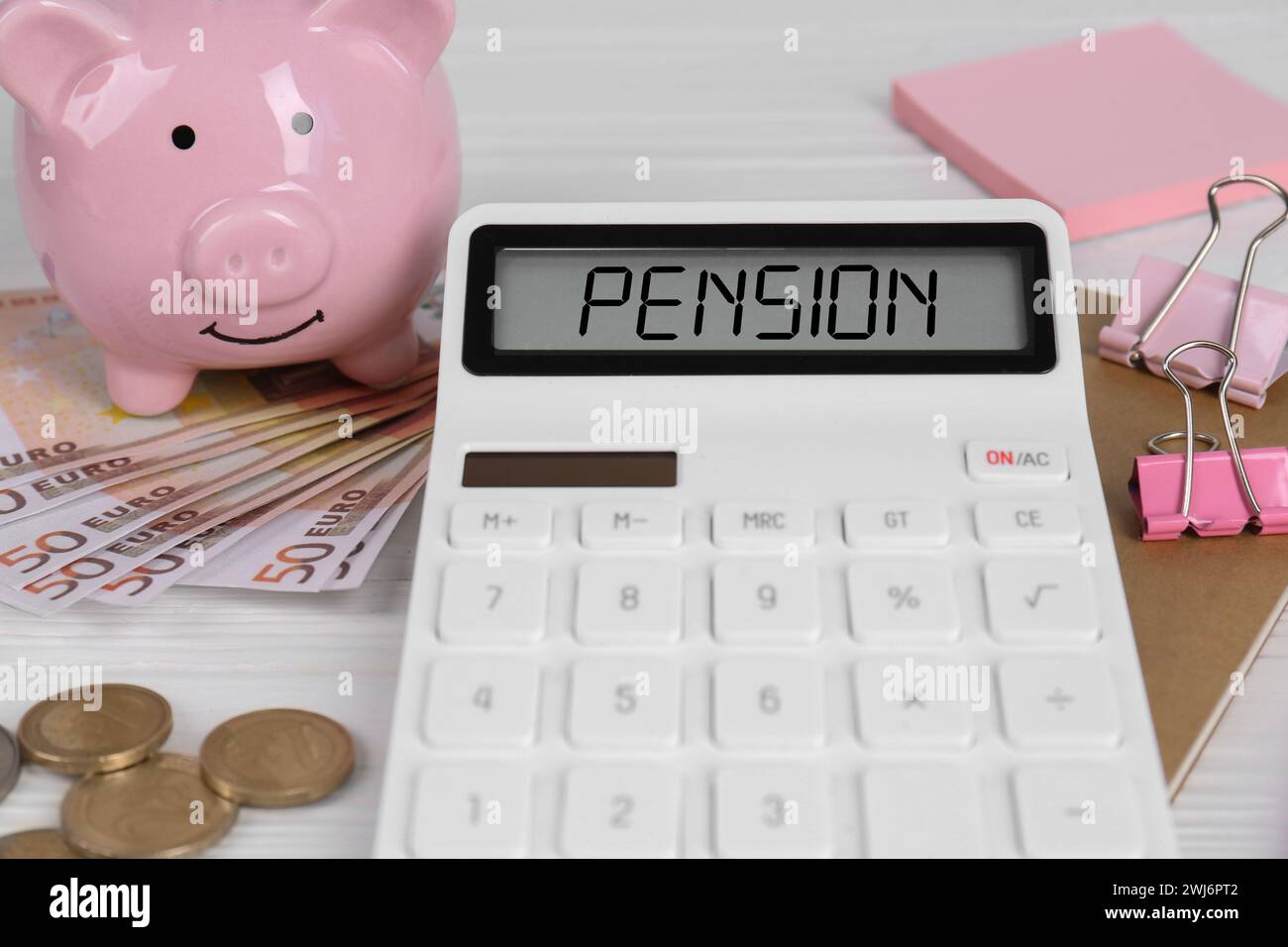 Calculatrice avec mot pension, argent, tirelire et papeterie sur table en bois blanc, gros plan Banque D'Images