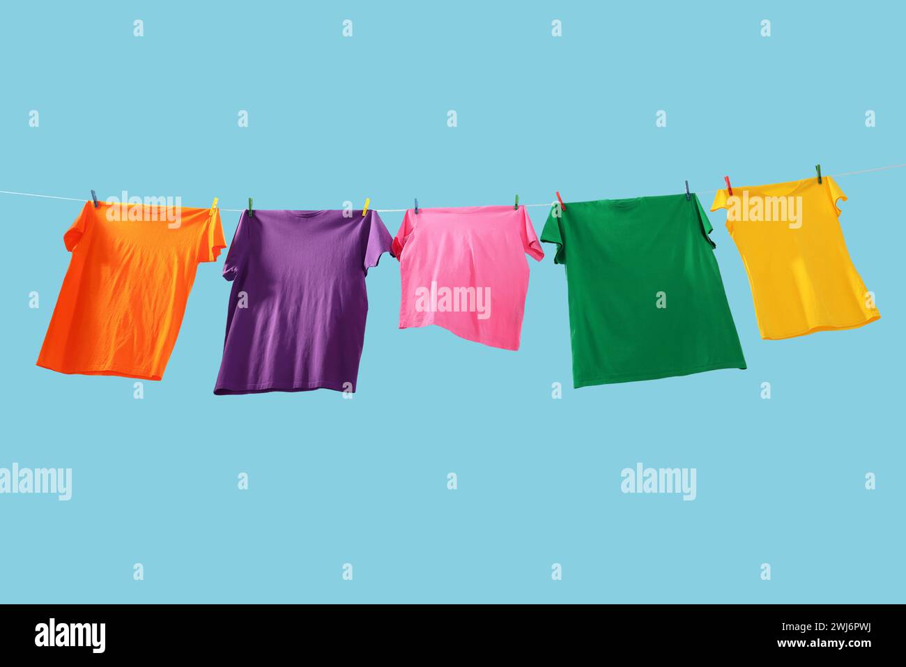 T-shirts colorés séchant sur la ligne de lavage sur fond bleu clair, vue d'angle bas Banque D'Images T-shirts colorés séchant sur la ligne de lavage sur fond bleu clair, vue d'angle bas Banque D'Images