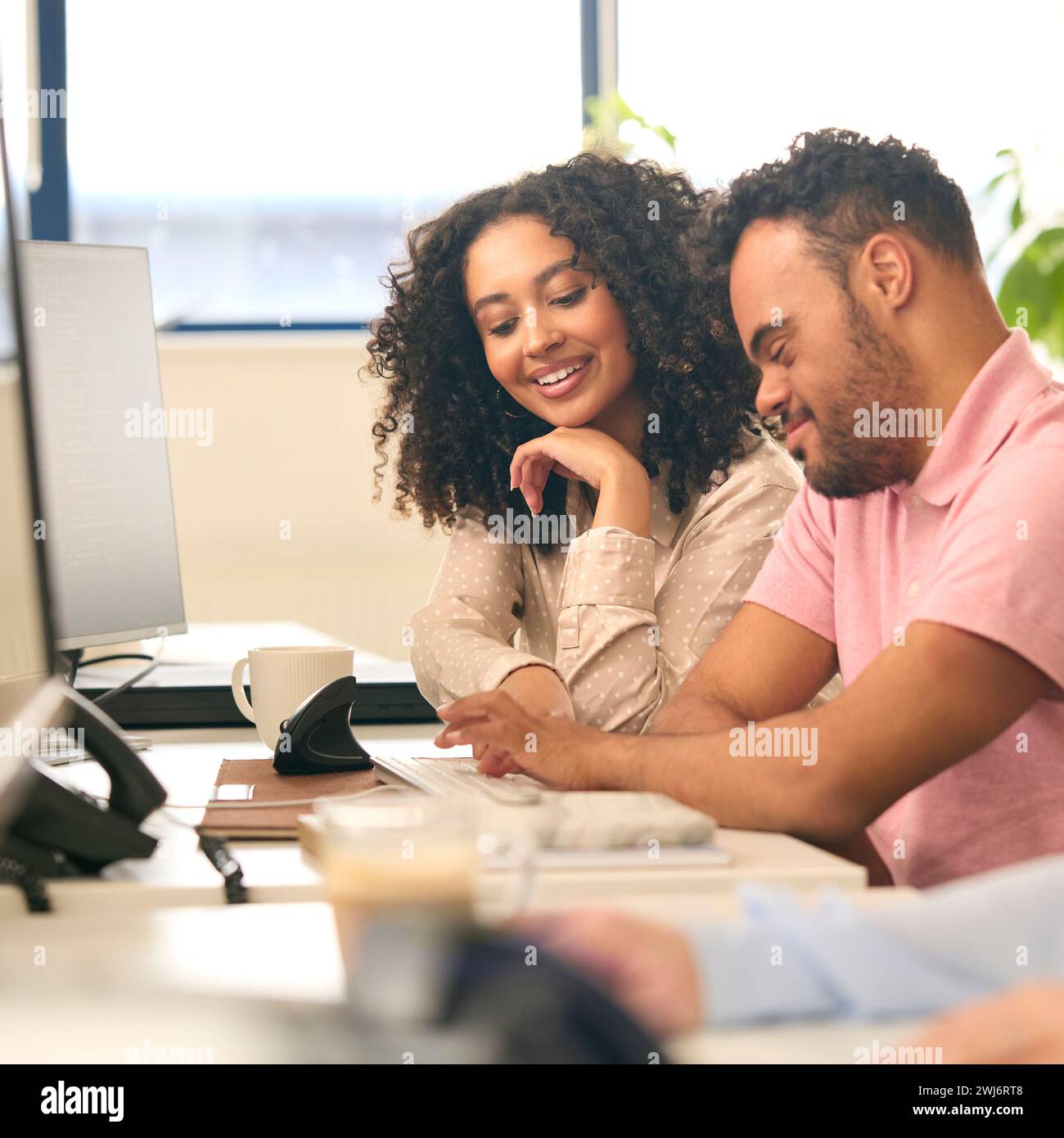 Femme travaillant dans Office Based Business Training Man with Down syndrome à l'aide d'un ordinateur Banque D'Images