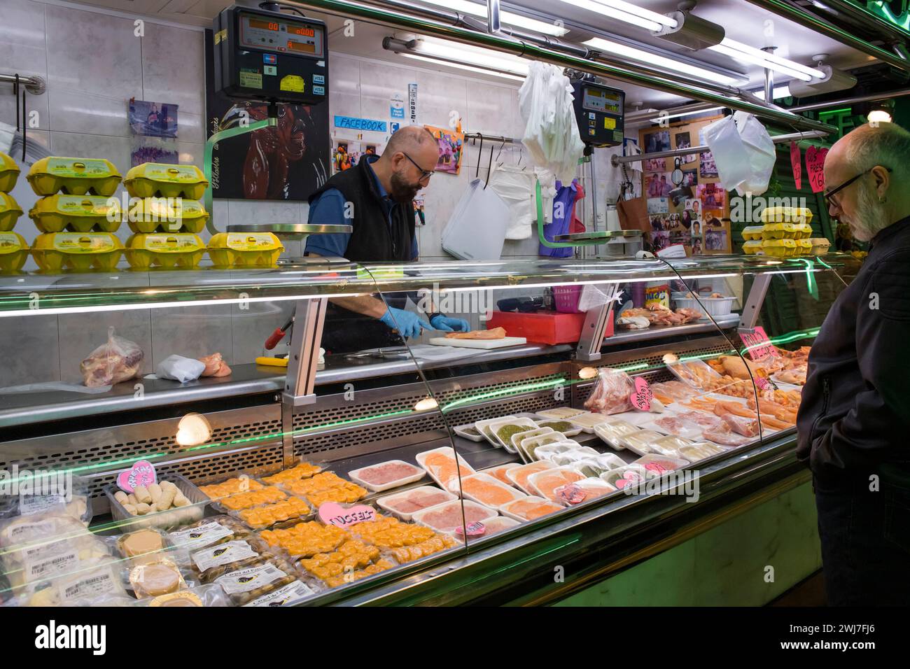 Poultryman coupe un morceau de poulet pour un client dans l'ancien marché central d'Abaceria de Barcelone Banque D'Images