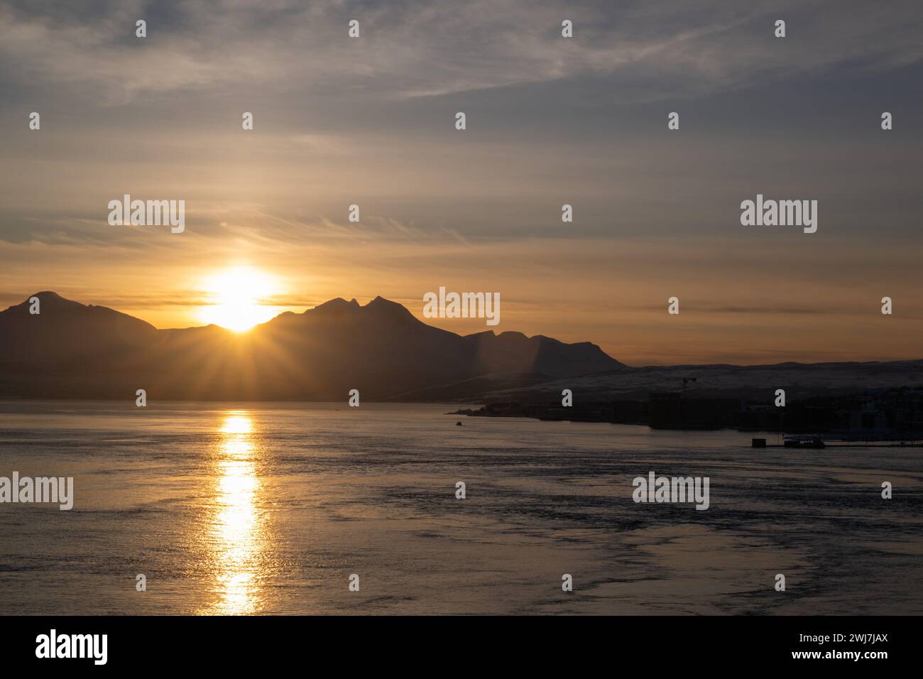 Le soleil se couchant derrière les montagnes et jetant un reflet doré sur l'eau calme de l'Arctique. Banque D'Images