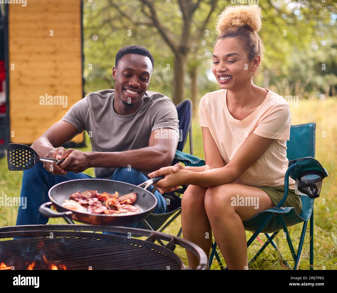 Couple Camping à la campagne avec RV Cooking Bacon et œufs pour le petit déjeuner en plein air sur le feu Banque D'Images