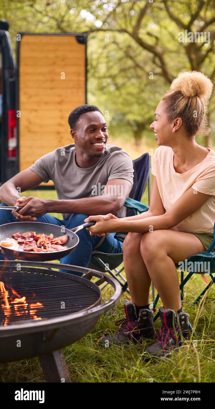 Couple Camping à la campagne avec RV Cooking Bacon et œufs pour le petit déjeuner en plein air sur le feu Banque D'Images