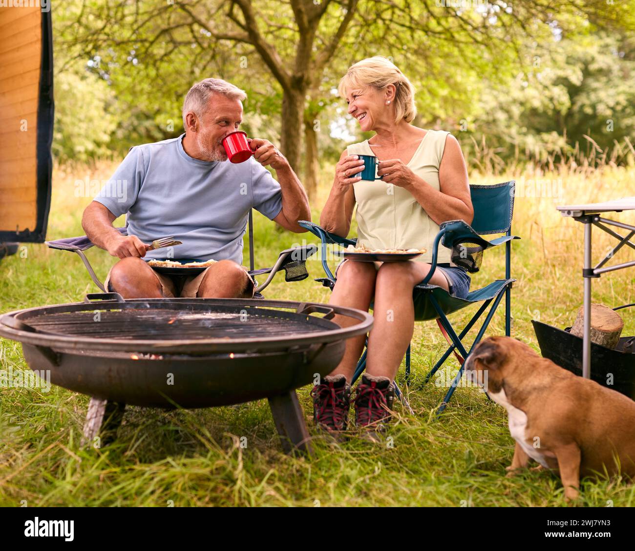 Couple senior avec Pet Dog Camping dans RV manger du bacon et des œufs pour le petit déjeuner en plein air sur le feu Banque D'Images