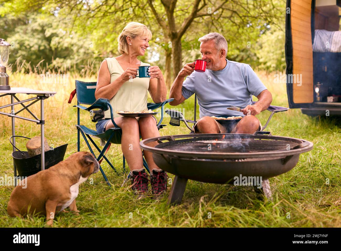 Couple senior avec Pet Dog Camping dans RV manger du bacon et des œufs pour le petit déjeuner en plein air sur le feu Banque D'Images