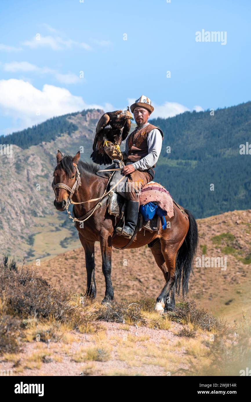 Chasseur traditionnel d'aigle kirghize avec aigle dans les montagnes, chassant à cheval devant un paysage sec, près de Kysyl-Suu, Issyk Kul, Kirghizistan, AS Banque D'Images