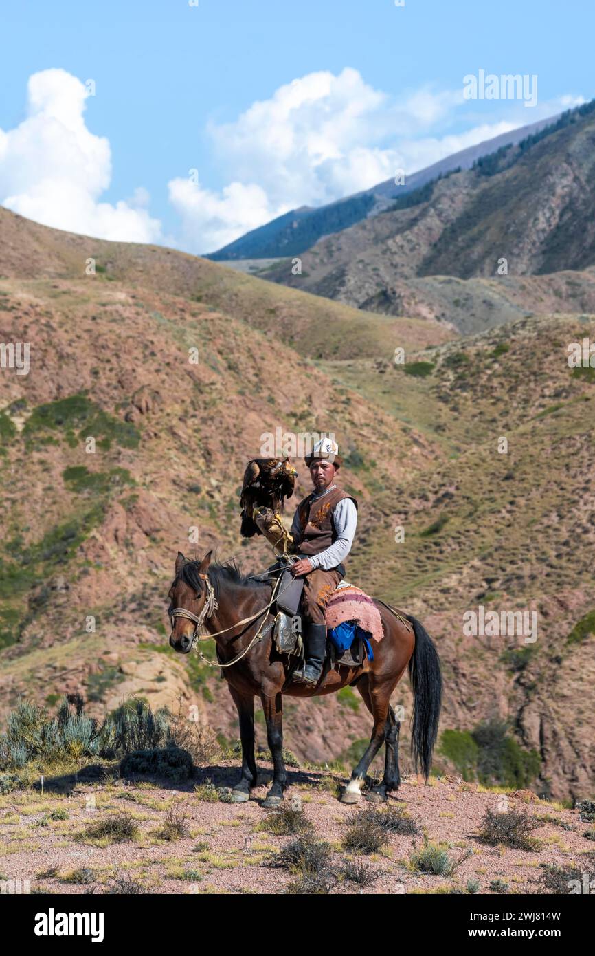 Chasseur traditionnel d'aigle kirghize avec aigle dans les montagnes, chassant à cheval devant un paysage sec, près de Kysyl-Suu, Issyk Kul, Kirghizistan Banque D'Images