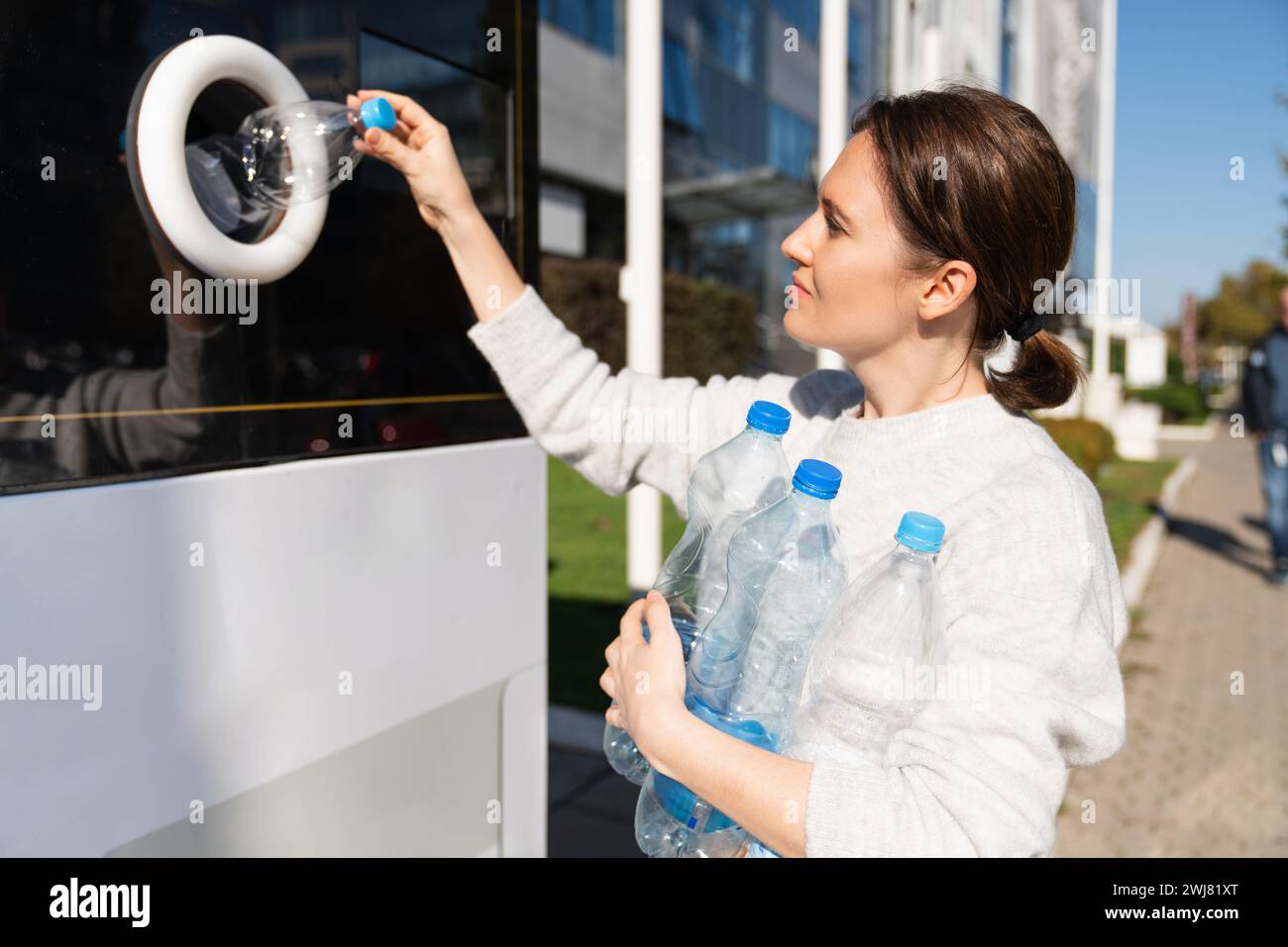 La femme utilise une machine en libre-service pour recevoir des bouteilles et des canettes en plastique usagées dans une rue de la ville. Banque D'Images