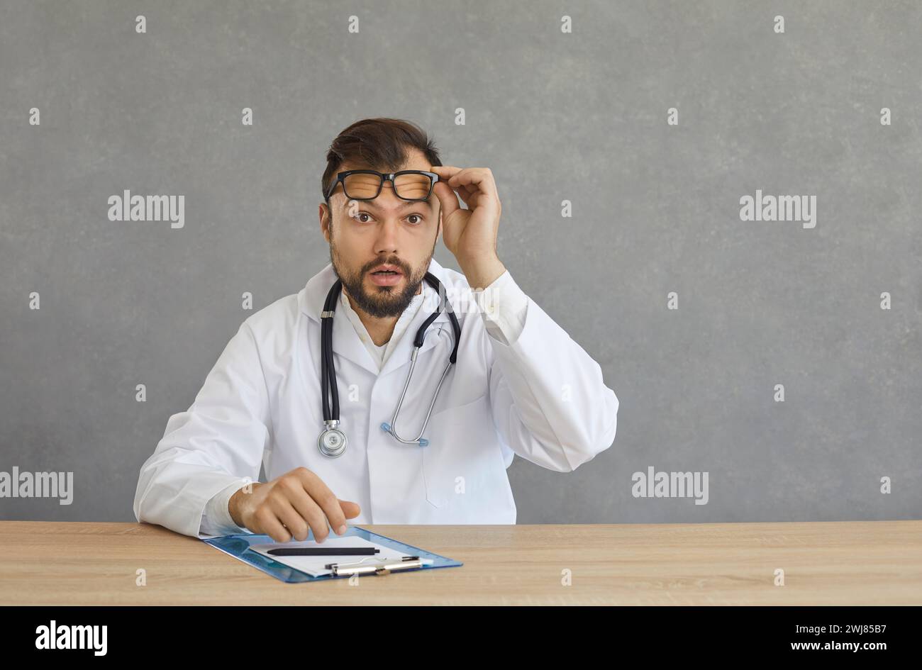 Un médecin thérapeute d'âge moyen choqué retire des lunettes et regarde la caméra Banque D'Images