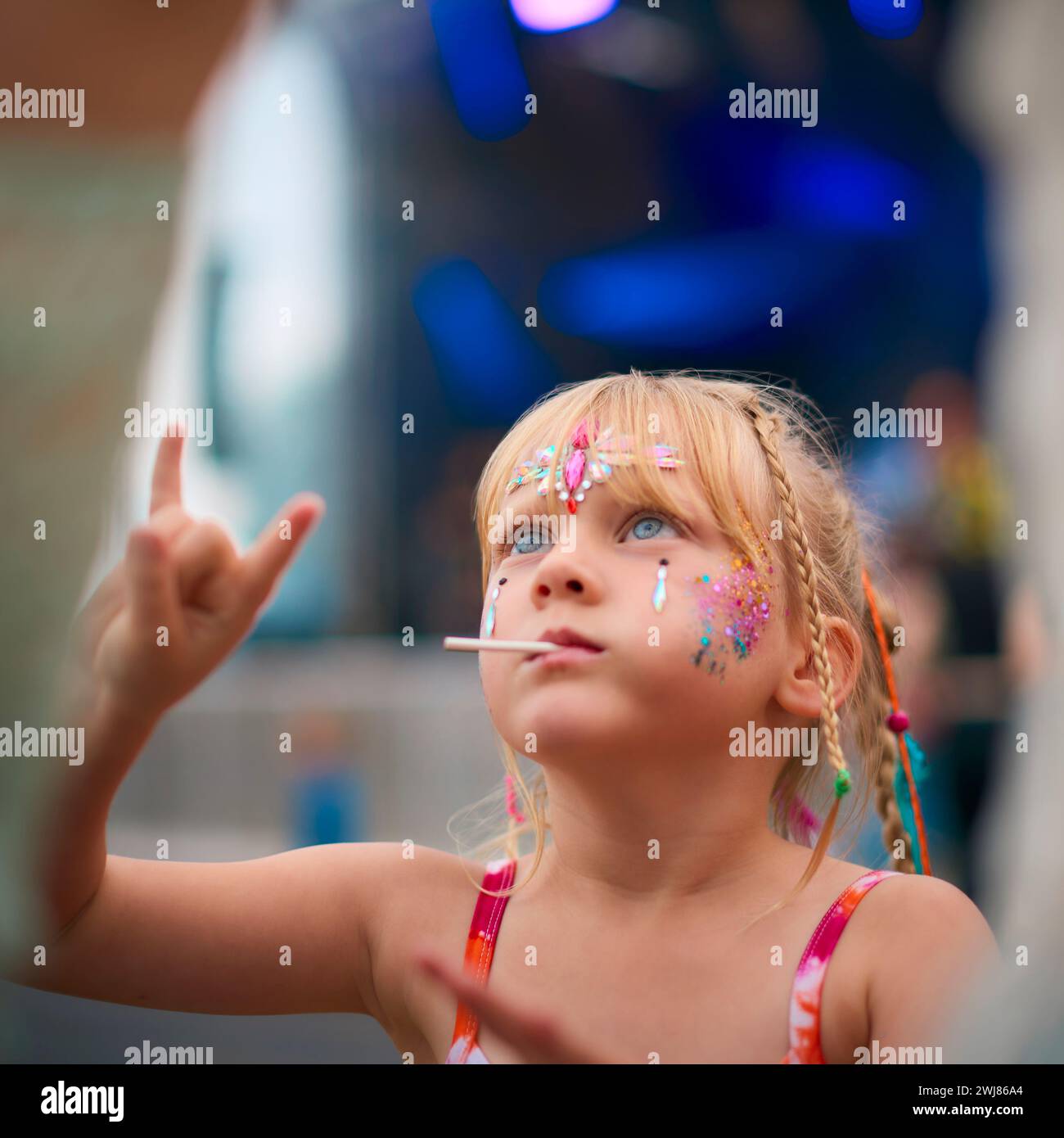 Fille assise sur les épaules de ses parents faisant un geste de main Rock and Roll au Festival de musique d'été en plein air Banque D'Images