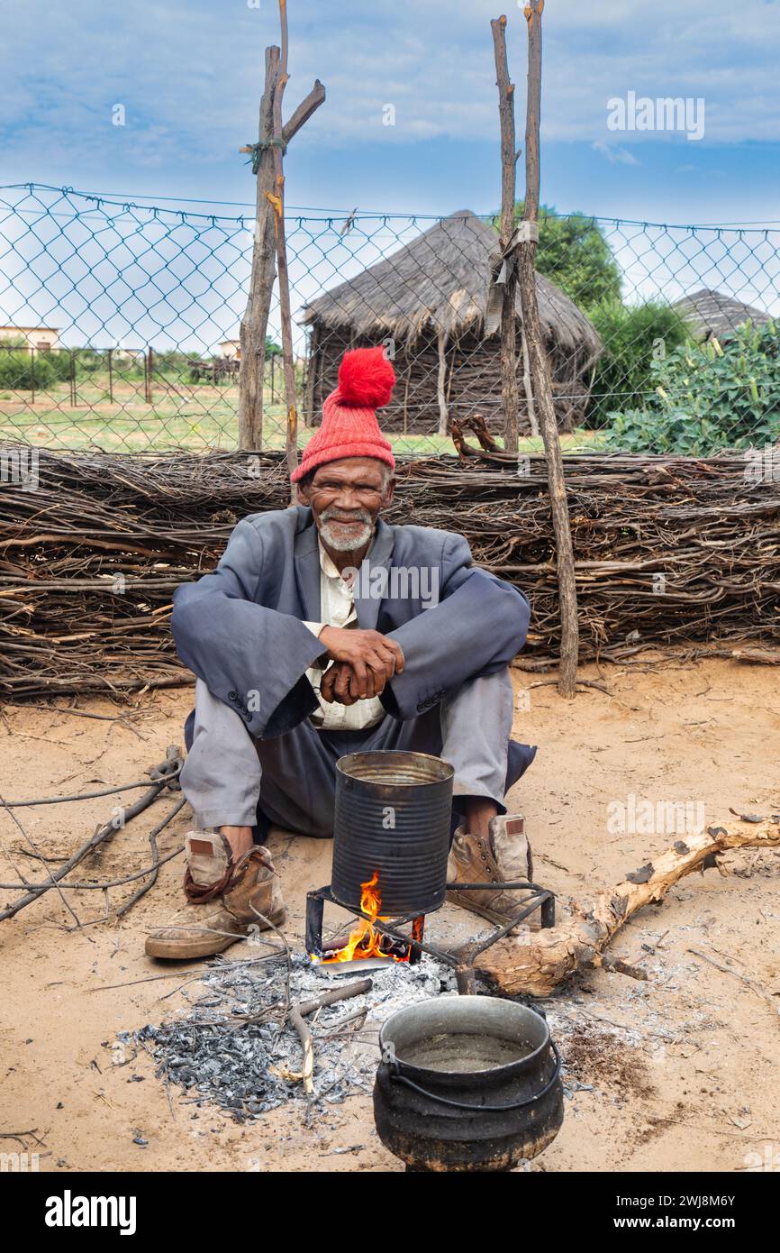 vieil homme africain dans le village, debout dans la cour dans la cuisine extérieure, maisons de boue avec toit de chaume en arrière-plan Banque D'Images