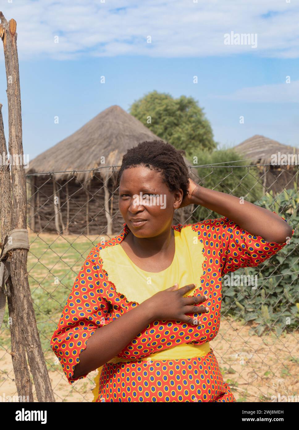 femme africaine dans le village, robe traditionnelle, debout dans la cour, maisons de boue avec toit de chaume en arrière-plan Banque D'Images
