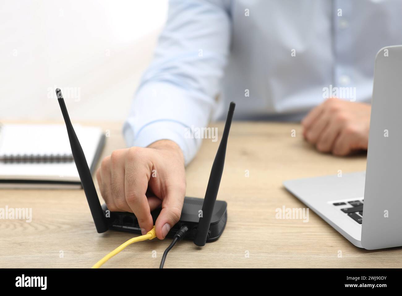 Homme insérant le câble dans le routeur Wi-Fi à la table en bois à l'intérieur, gros plan Banque D'Images