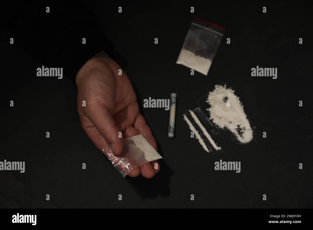 Toxicomanie. Homme avec de la cocaïne et un billet roulé d'un dollar à la table sombre, vue de dessus Banque D'Images