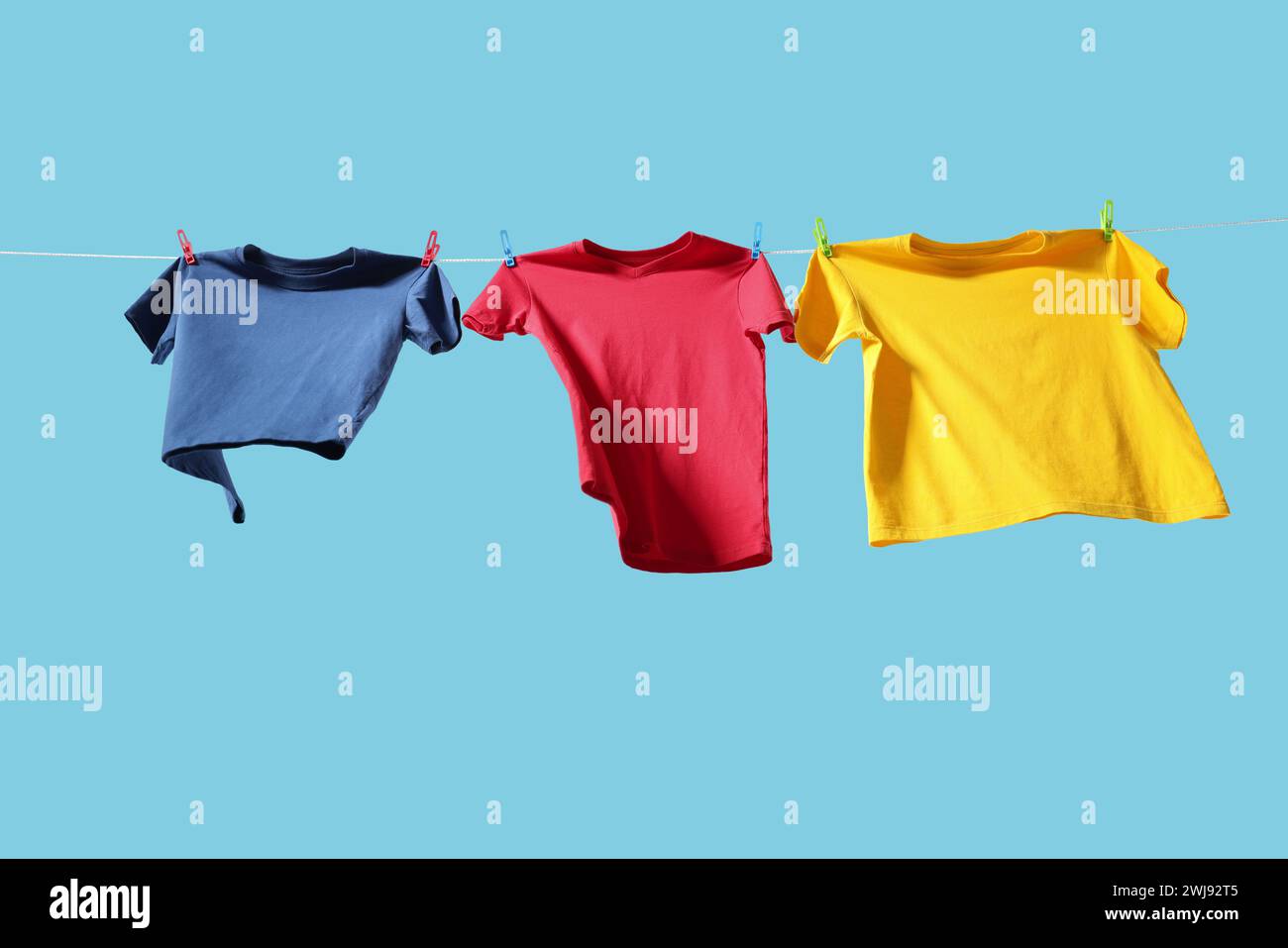 T-shirts colorés séchant sur la ligne de lavage sur fond bleu clair, vue d'angle bas Banque D'Images T-shirts colorés séchant sur la ligne de lavage sur fond bleu clair, vue d'angle bas Banque D'Images