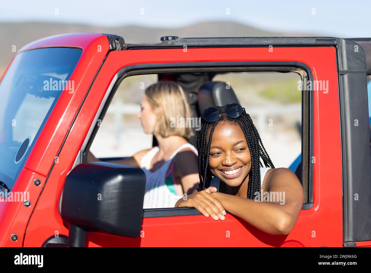 Deux femmes partagent la joie lors d’un Road trip ensoleillé dans une jeep rouge. Banque D'Images