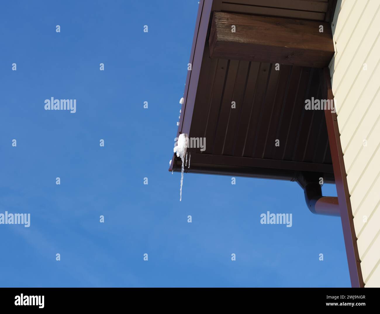 Le bord du toit avec un peu de neige et de glaçons contre le ciel bleu Banque D'Images