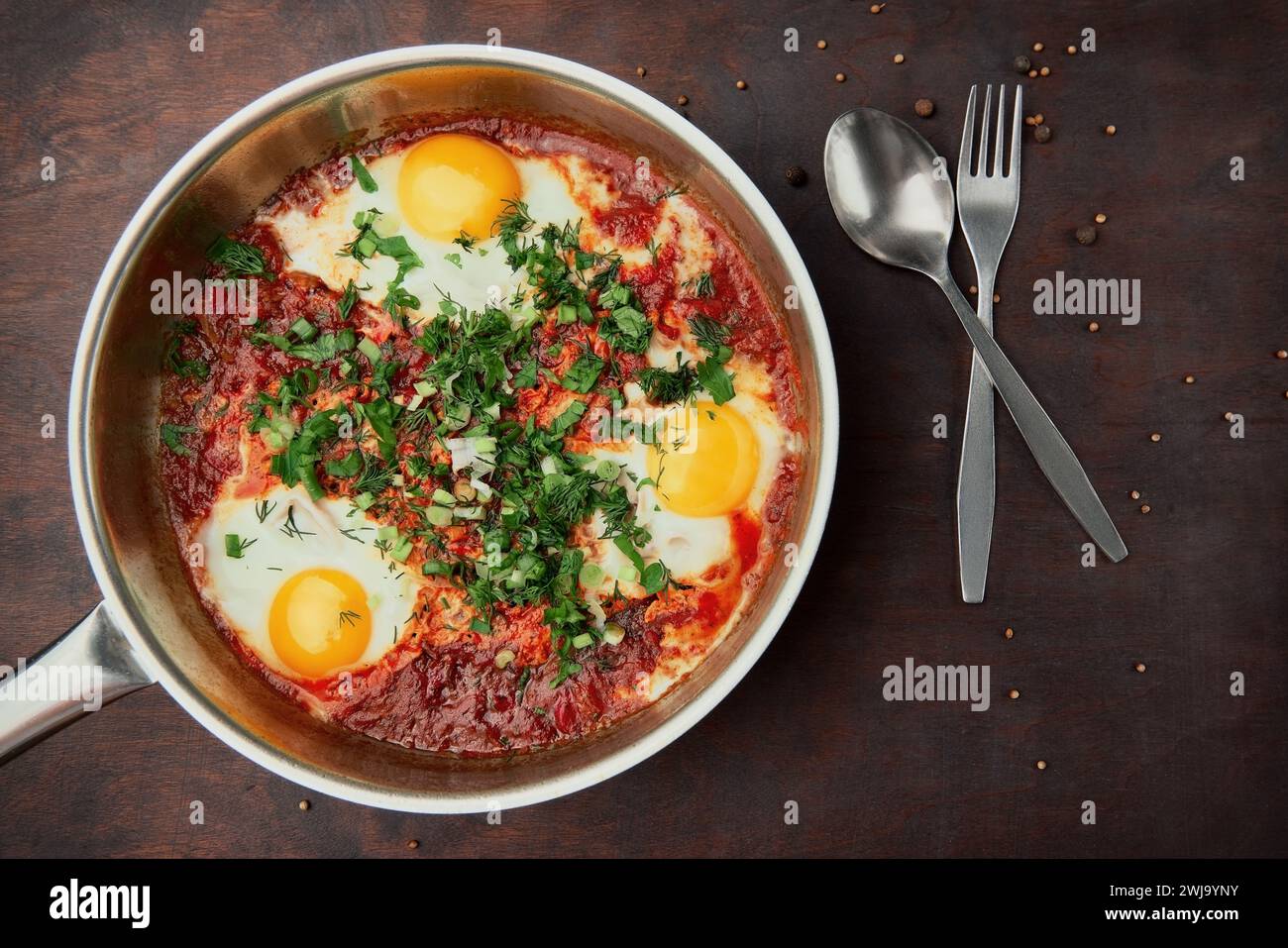 Shakshuka savoureux et sain, omelette du Moyen-Orient dans une poêle. Délicieux œufs brouillés cuits dans une sauce tomate-poivre épicée sur une languette en bois rugueuse Banque D'Images