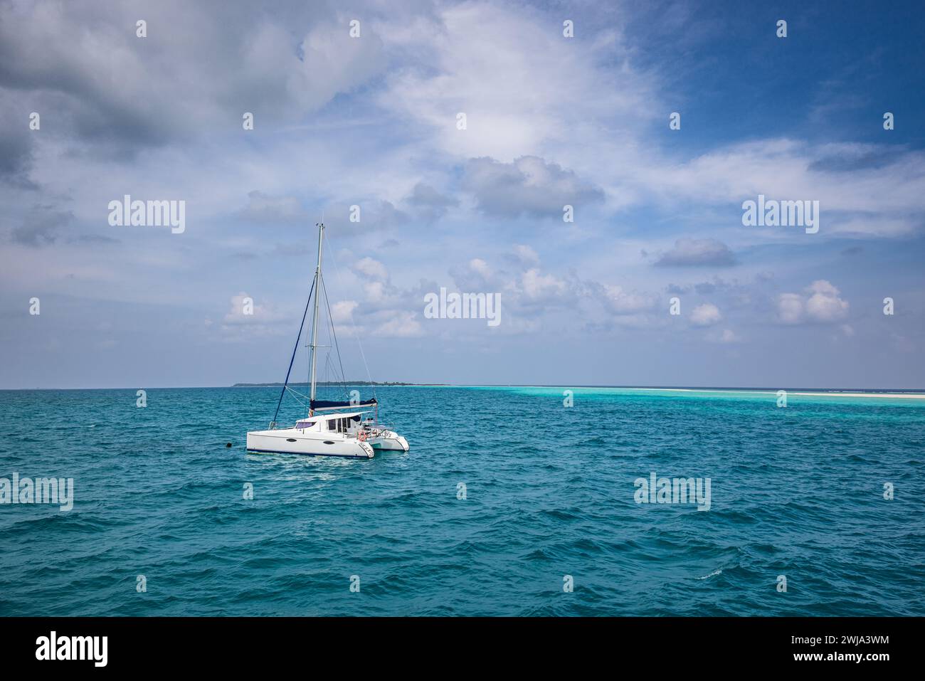 Belle eau turquoise autour d'un voilier de luxe blanc ancré au milieu de l'océan. Ciel nuageux, lagon océanique. Voyage d'aventure, paysage marin récréatif Banque D'Images