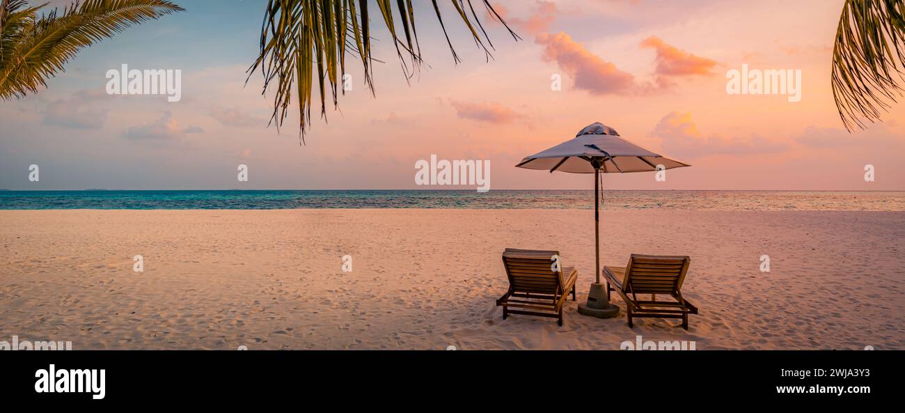 Magnifique coucher de soleil tropical, deux chaises longues, parasol sous le palmier. Sable blanc, vue sur la mer avec horizon, ciel crépuscule coloré, calme Banque D'Images
