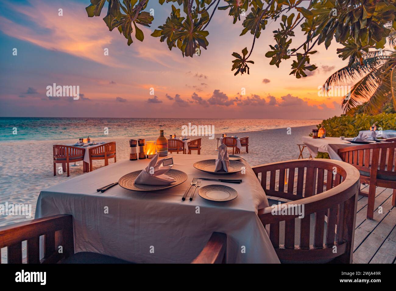 Restaurant extérieur à la plage. Table au restaurant tropical Beach. Bougies lumineuses LED et tables en bois, chaises sous un beau ciel de coucher de soleil Banque D'Images
