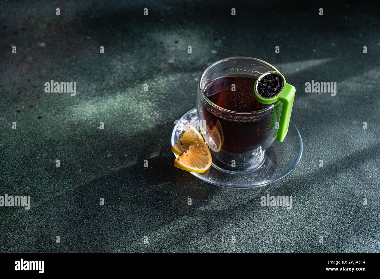 Du haut d'un verre de thé clair avec une tranche de citron et une passoire de thé vert sur un fond sombre texturé Banque D'Images