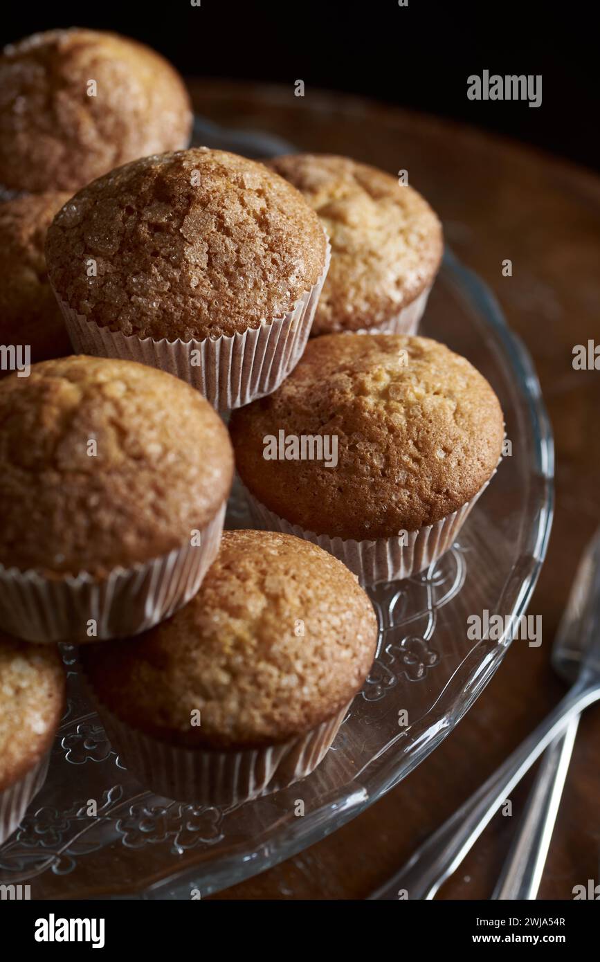 Gros plan de muffins brun doré disposés sur une assiette de service décorative en verre, avec un fond sombre. Banque D'Images