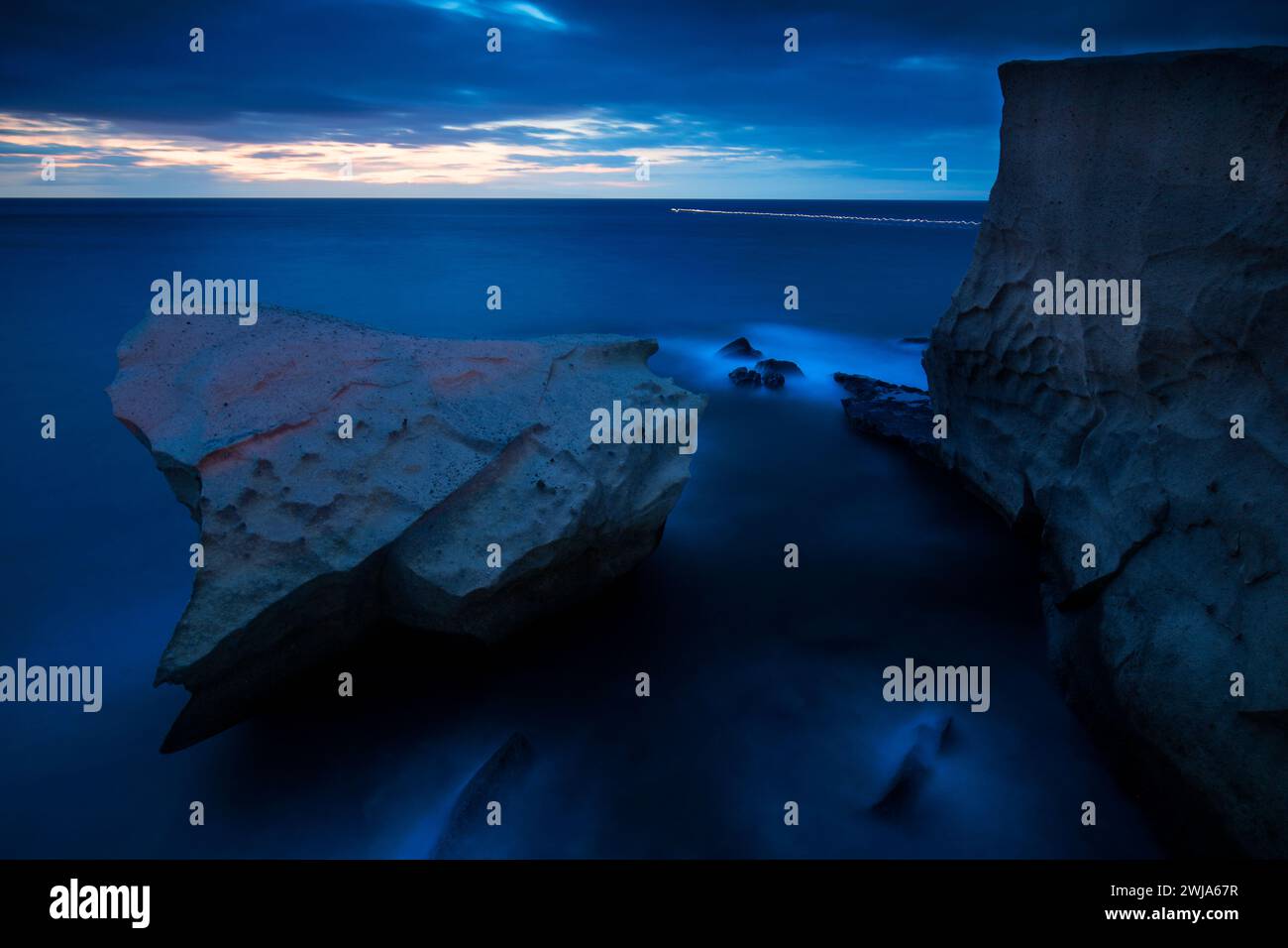 Un paysage marin tranquille au crépuscule mettant en vedette d'imposantes falaises contre un océan bleu et calme sous un ciel doux et nocturne Banque D'Images