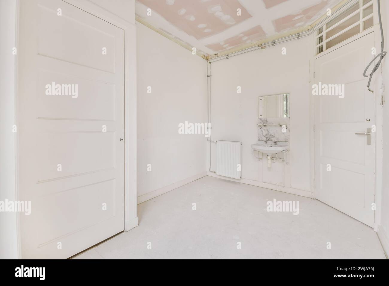 Une pièce vide en cours de rénovation, avec des murs blancs et un plafond apparent et non fini avec câblage électrique visible. Banque D'Images
