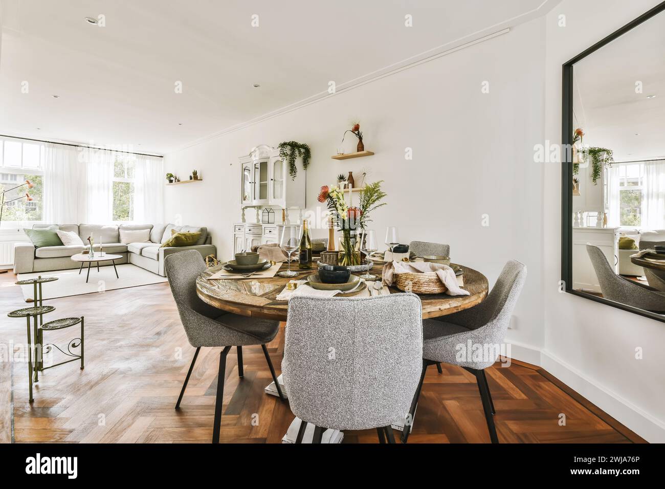 Une salle à manger élégamment décorée avec une table ronde en bois, des chaises modernes et un espace de vie élégant en arrière-plan. Banque D'Images