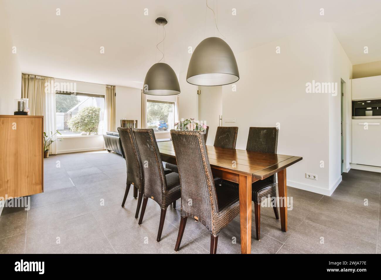 Un coin repas moderne lumineux et spacieux comprend une table en bois, des chaises en osier et des lampes suspendues élégantes. Banque D'Images
