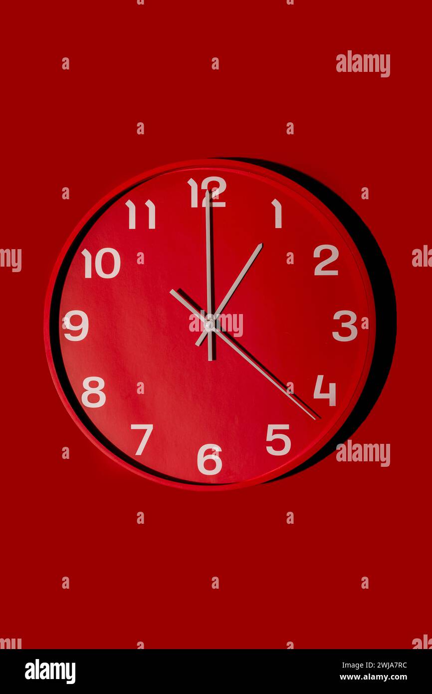 Une horloge murale rouge moderne présente un design simpliste sur un fond rouge monochrome, soulignant le minimalisme et l'harmonie des couleurs Banque D'Images