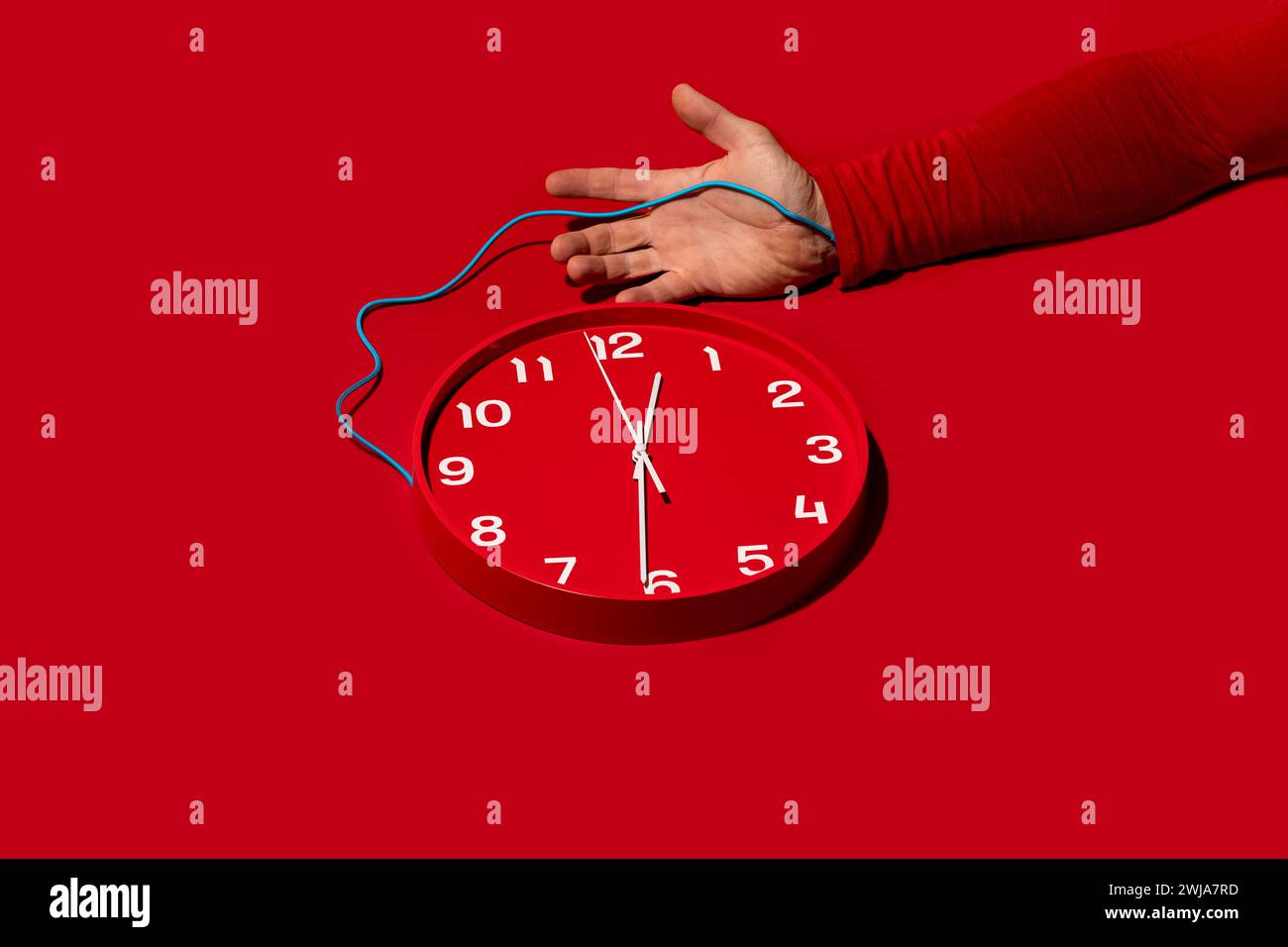 Le bras d'une personne dans une manche rouge est câblé à une horloge rouge, faisant référence à la gestion ou au contrôle du temps Banque D'Images