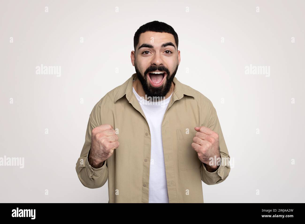 Heureux choqué beau jeune latin gagnant avec la barbe dans le décontracté avec la bouche ouverte Banque D'Images