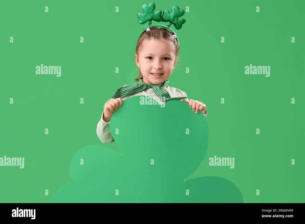 Petite fille mignonne avec bandeau de nouveauté et feuille de trèfle sur fond vert. Prog Célébration de la fête de Patrick Banque D'Images