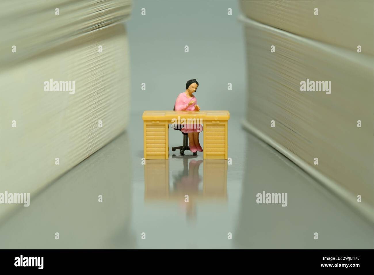 Miniature Tiny People jouet figure photographie. Une femme siège bibliothécaire sur le bureau dans l'allée de la bibliothèque. Photo d'image Banque D'Images