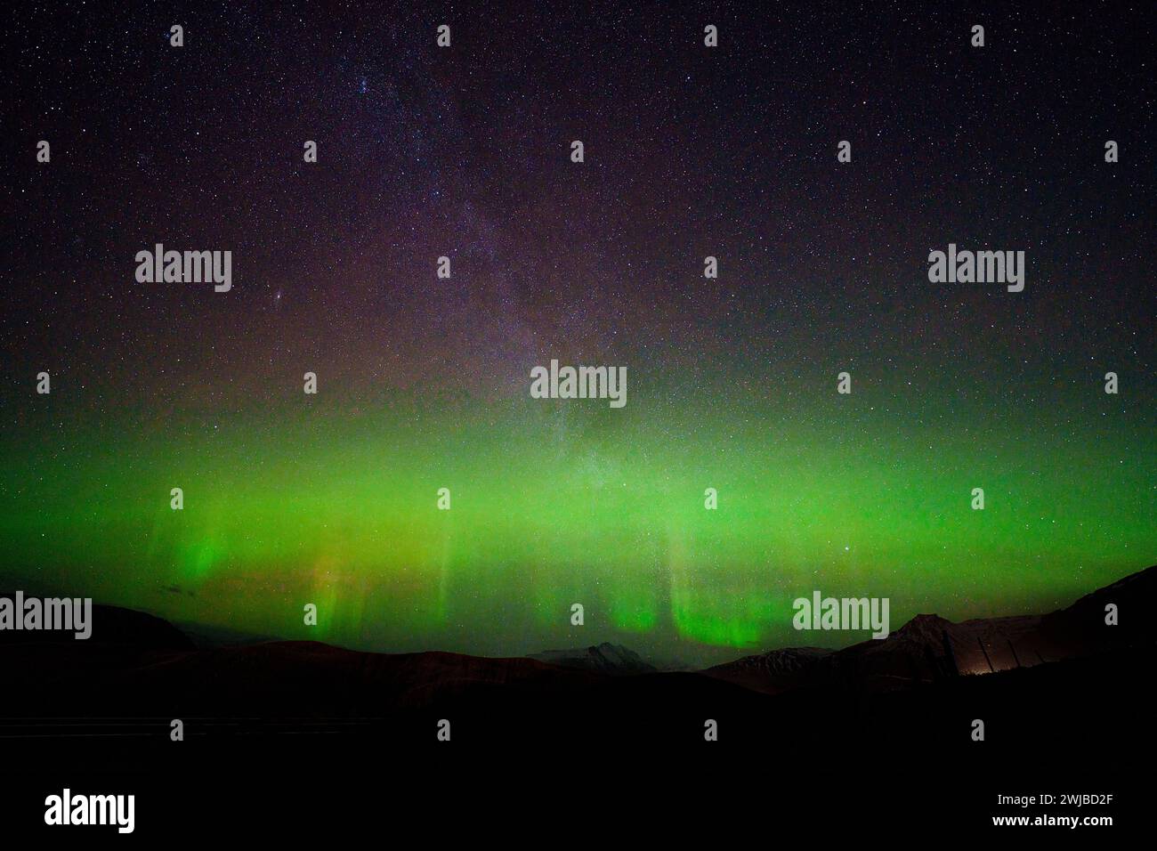 Aurore avec des piliers visibles entre les étoiles de la voie lactée au-dessus et les collines au-dessous. Une longue exposition fait ressortir les verts et les violets dans le ciel. Banque D'Images Aurore avec des piliers visibles entre les étoiles de la voie lactée au-dessus et les collines au-dessous. Une longue exposition fait ressortir les verts et les violets dans le ciel. Banque D'Images