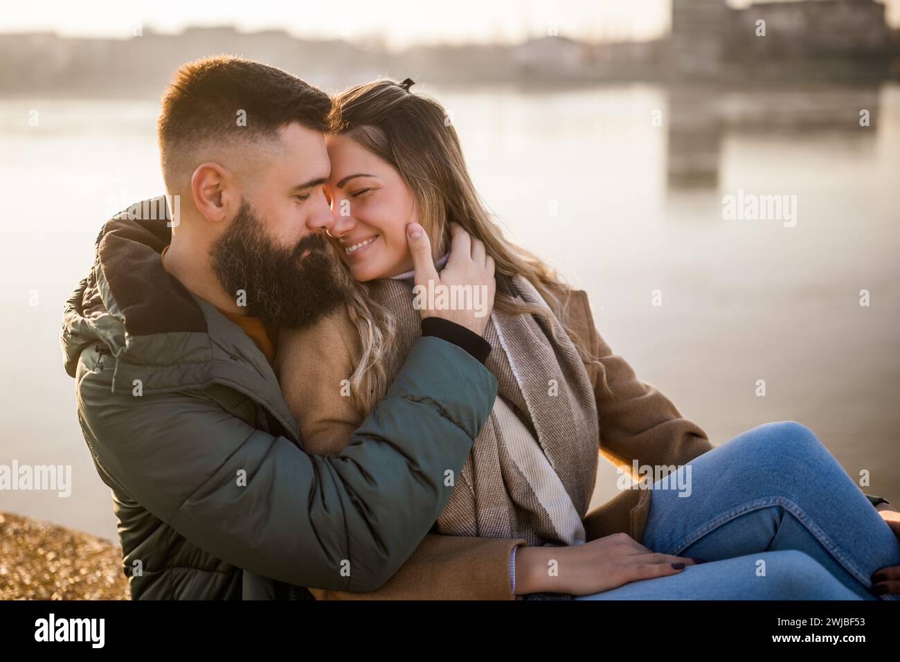 Heureux couple embrassant tout en appréciant assis au bord de la rivière. Banque D'Images