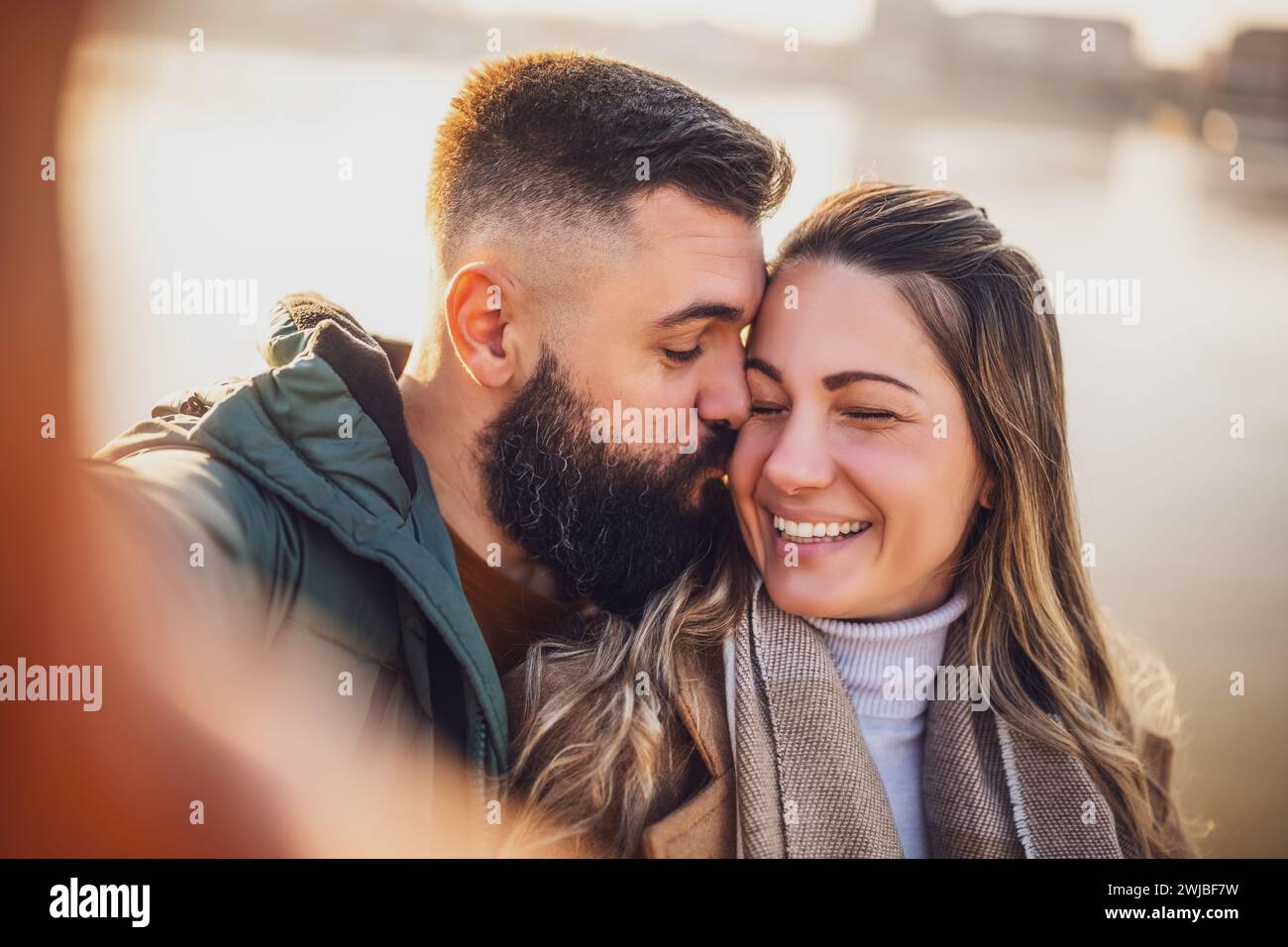 Gros plan d'un couple heureux prenant selfie en plein air. Homme embrassant sa femme dans la joue. Banque D'Images